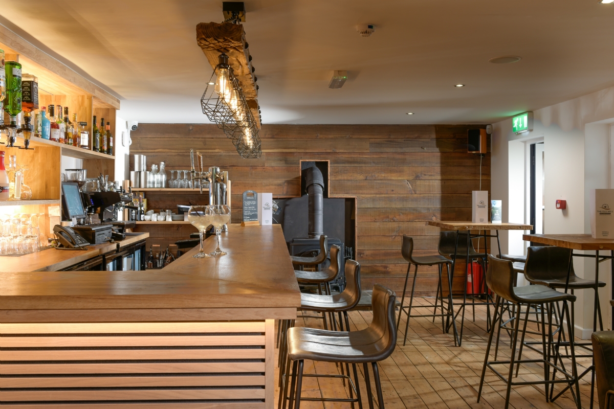 The bar at The Old Mill, reclaimed timber cladding, wood burner and high stools