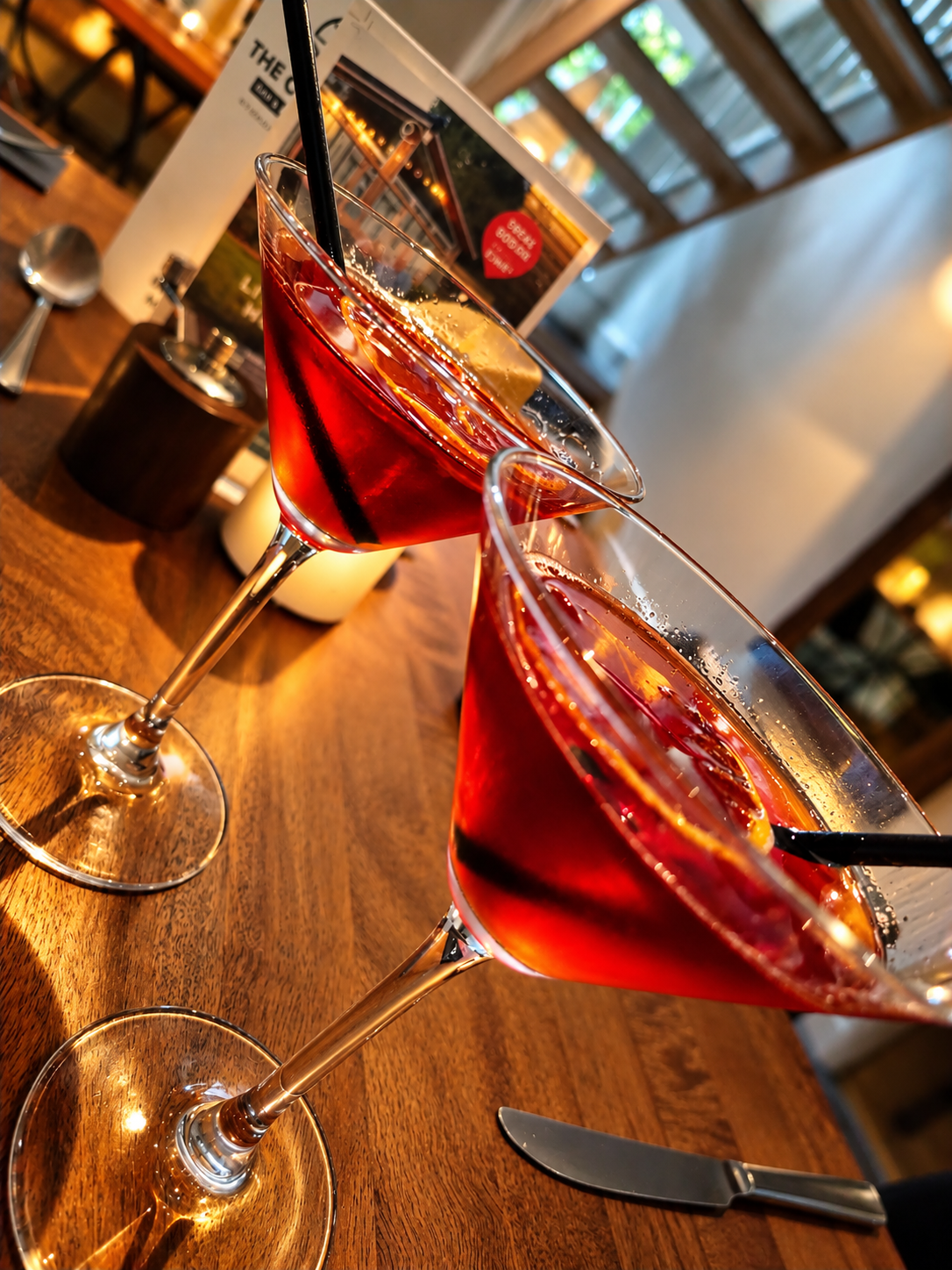 Two ruby-red cocktails in martini glasses with citrus garnish on a rustic table